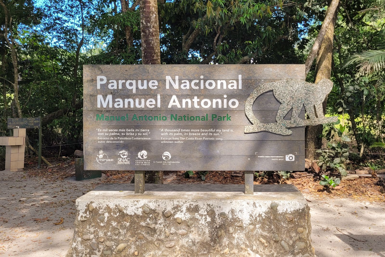 The wooden entrance sign for Parque Nacional Manuel Antonio, framed by rainforest trees at the park's trailhead