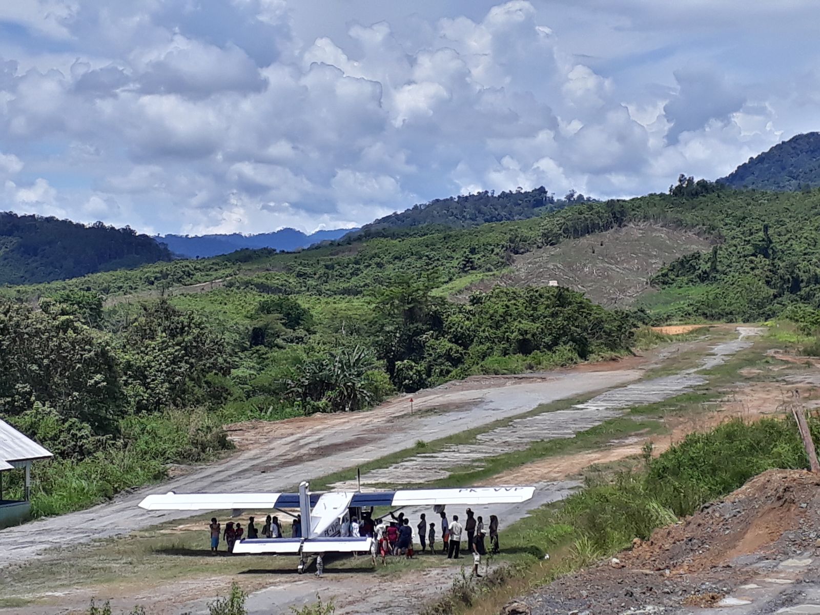 A small single-engine plane on a dirt airstrip cut into the rainforest, dense jungle canopy surrounding the runway