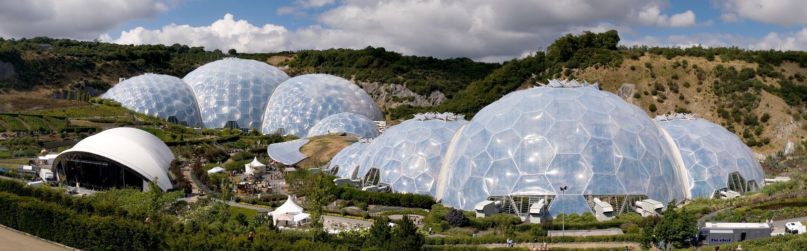 A geodesic glamping dome with a triangulated frame and part-clear, part-canvas panels, set up on a platform in dense jungle greenery