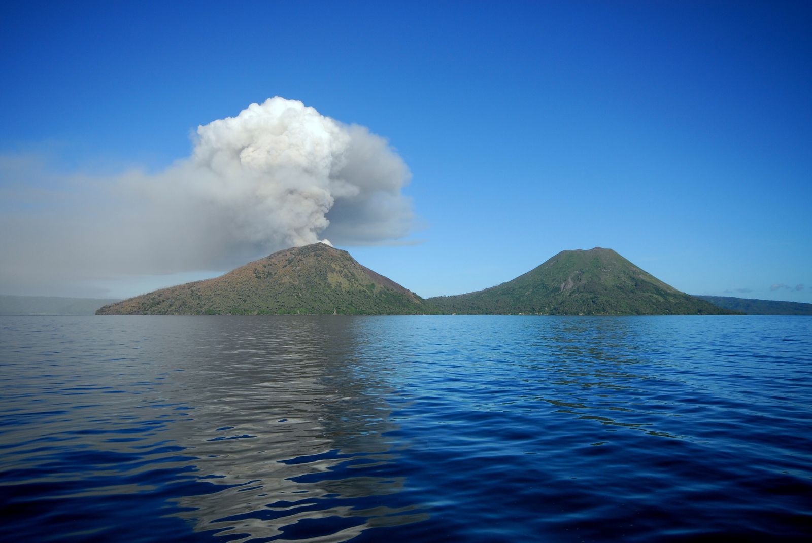 A rainforest hillside opening onto a distant volcano rising above the tree canopy, seen from a high jungle vantage point