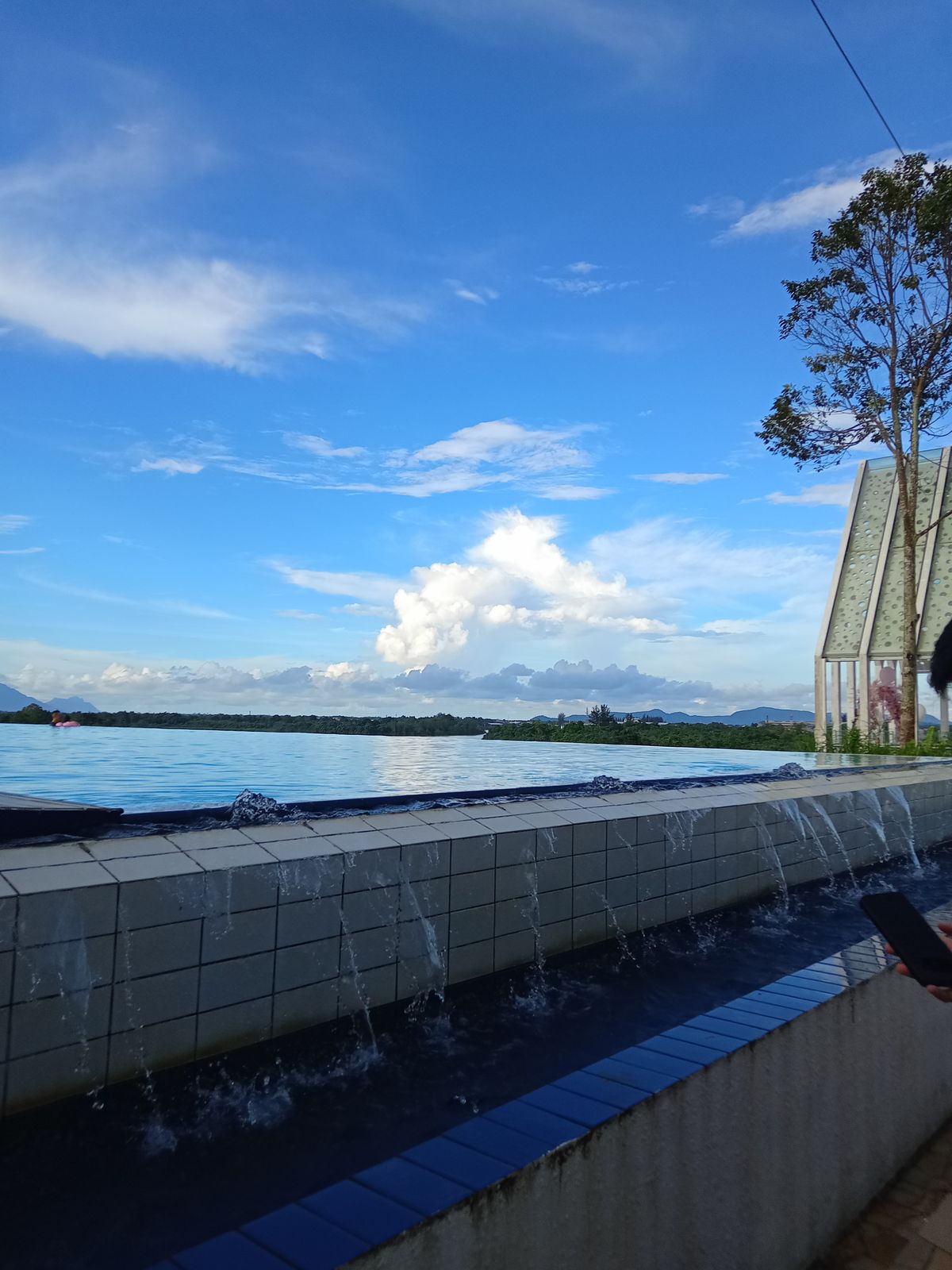 Infinity edge swimming pool with water spilling toward dense rainforest canopy below