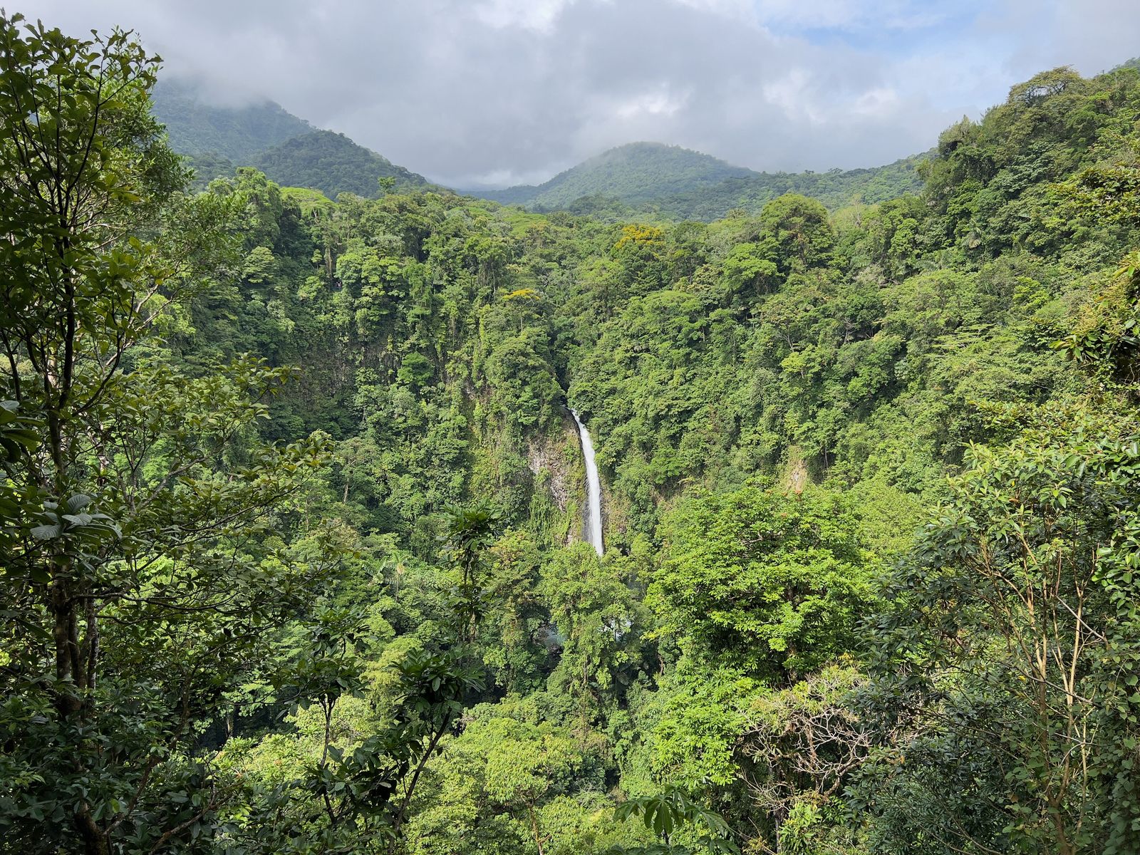 La Fortuna waterfall dropping through a deep forested canyon in Costa Rica, with cloud-wrapped mountains behind