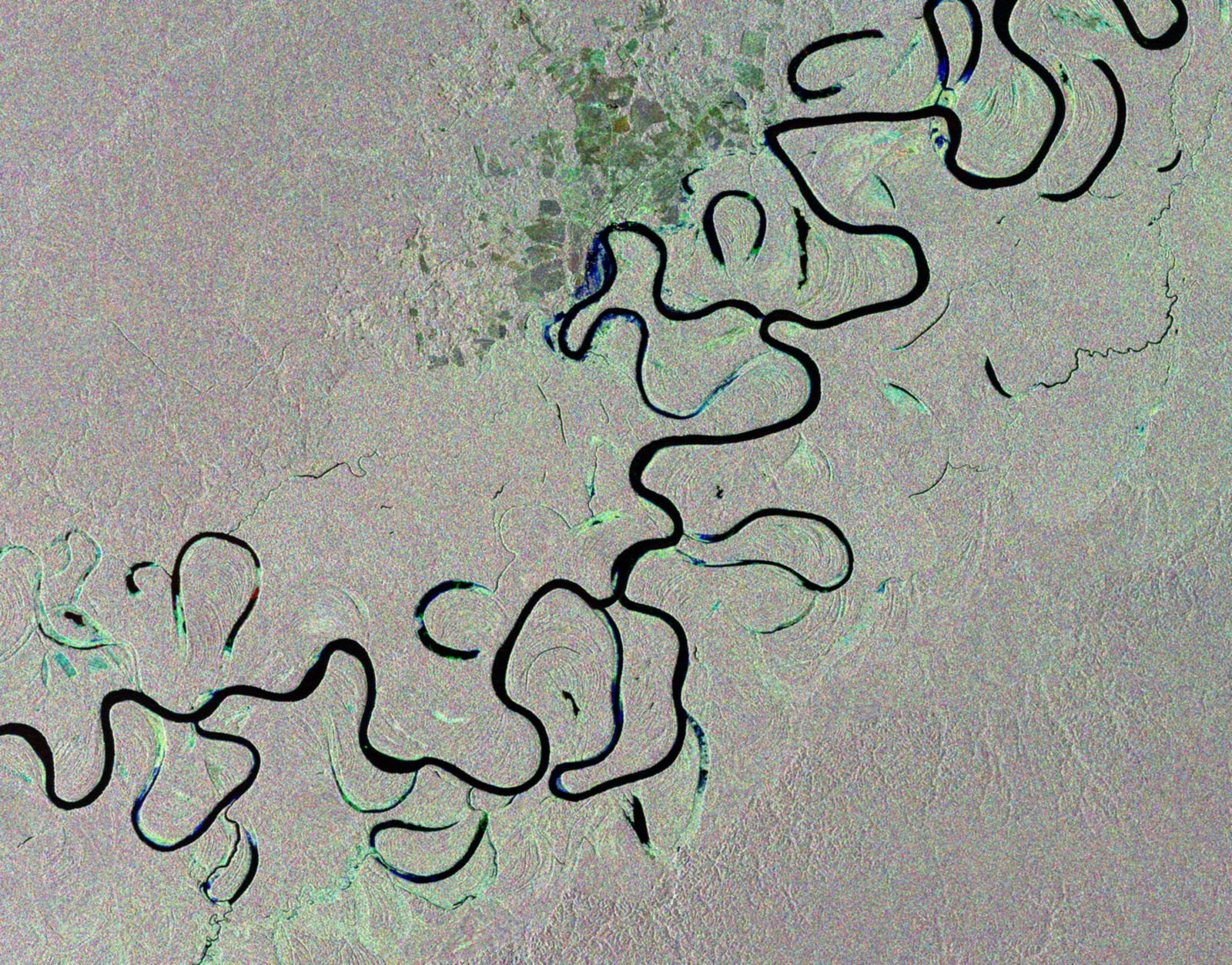 A wide, slow-moving tropical rainforest river bordered by dense green forest on both banks