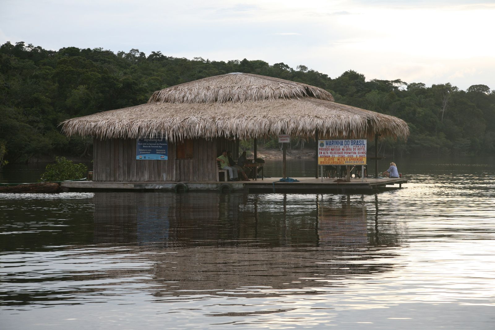 A wooden lodge structure on stilts over the dark water of the Rio Negro, surrounded by dense Amazon rainforest