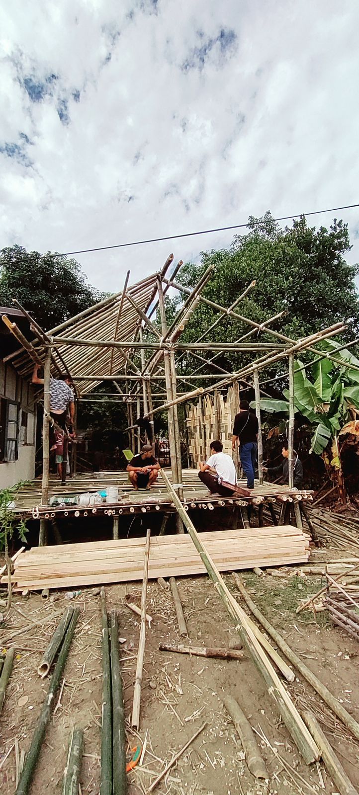 A bamboo house with a large triangular window framing the jungle and a stream below