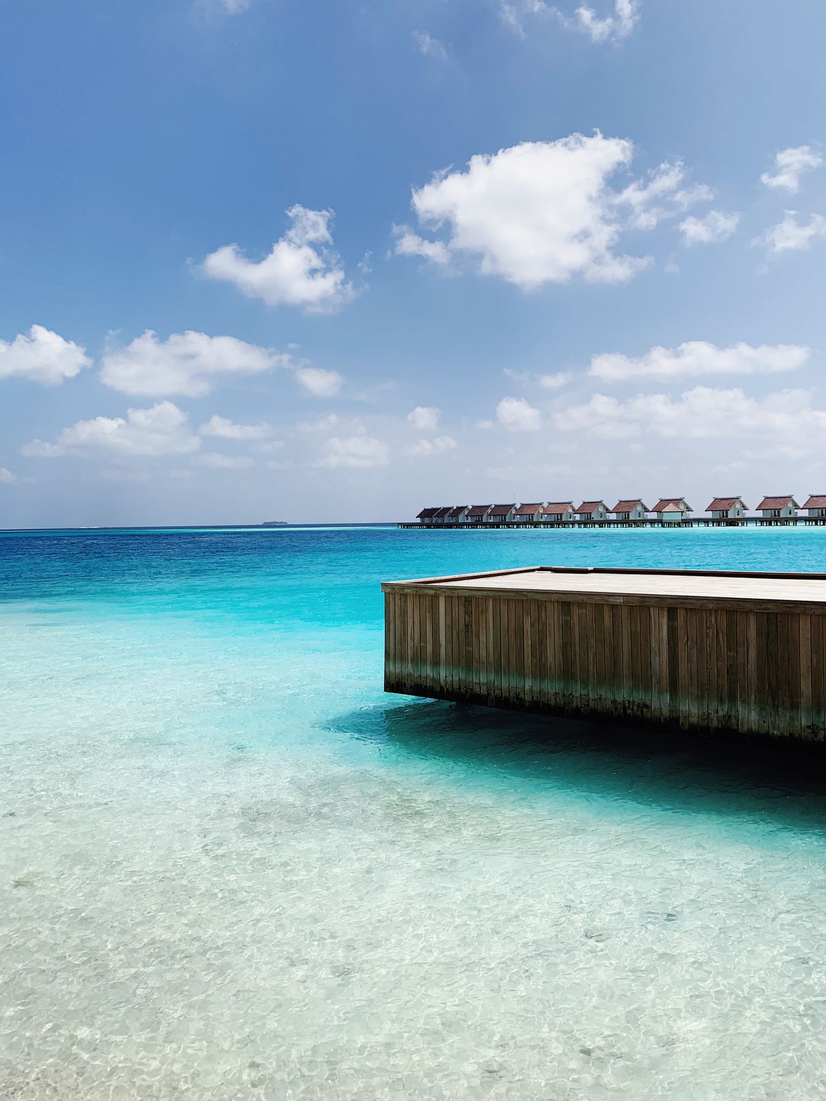A row of thatched-roof overwater bungalows on stilts over a clear tropical lagoon