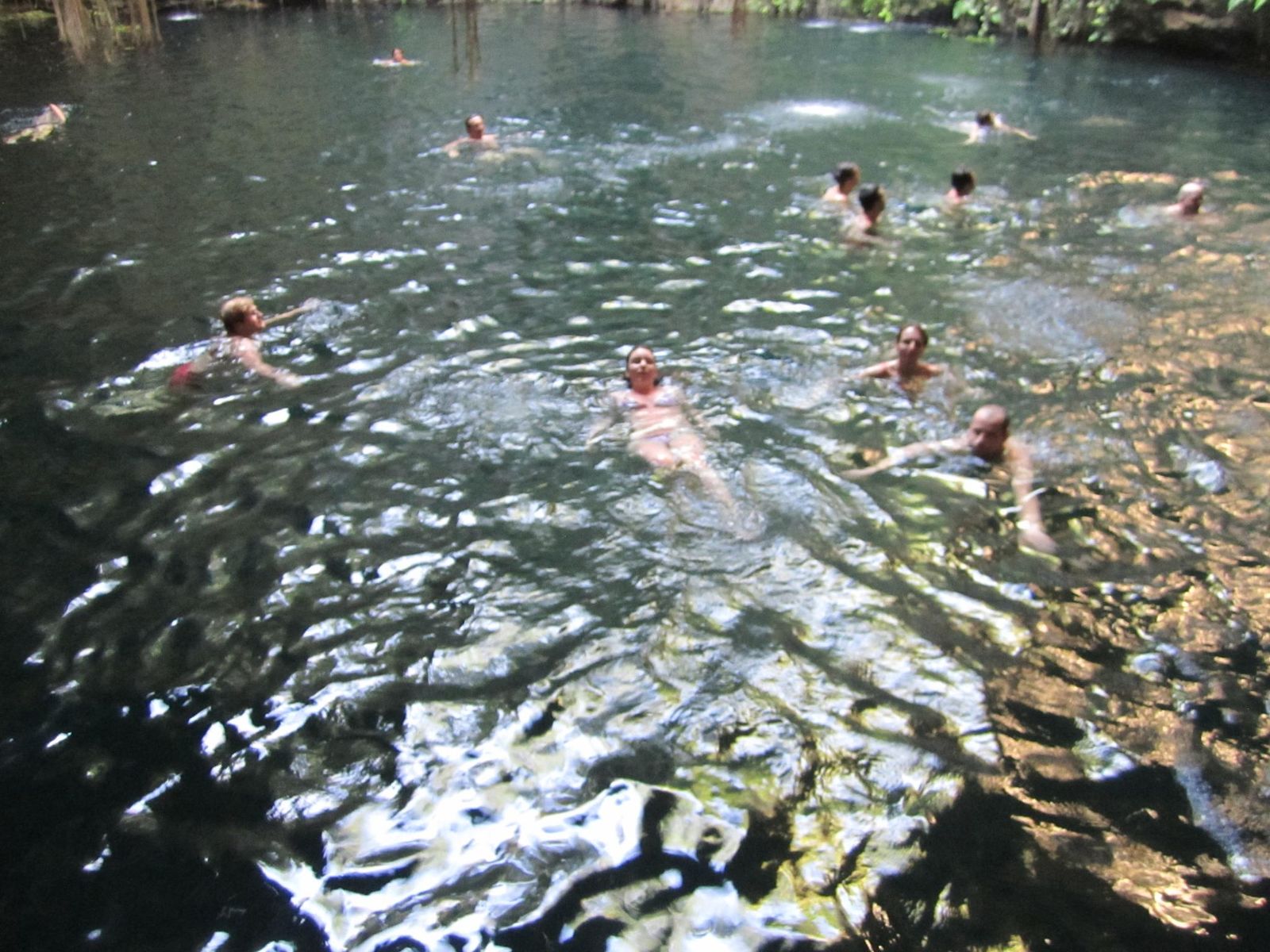 A clear turquoise cenote near Tulum, Mexico, with people swimming in the fresh water
