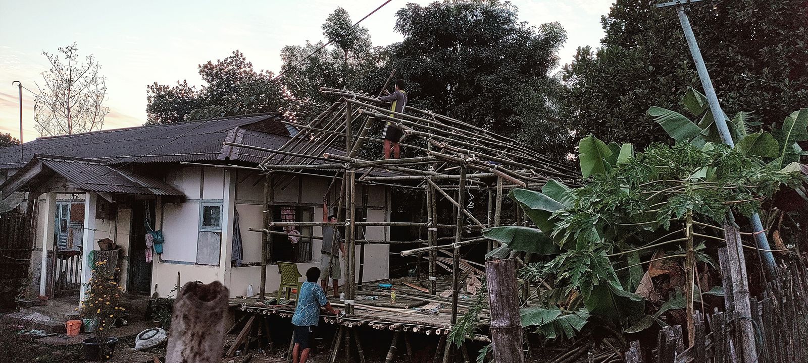 Workers lashing and pinning bamboo poles into a roof frame during the construction of a house