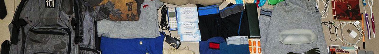An open travel backpack being packed with folded clothing and gear laid out beside it